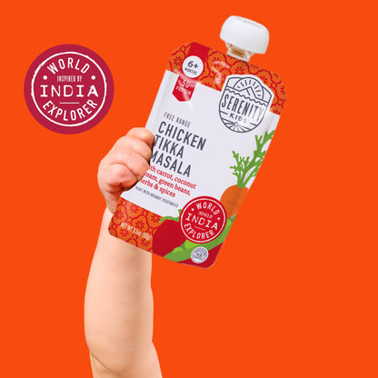 Hand holding a Serenity Kid's Chicken Tikka Masala pouch against an orange background with 'World Inspired India Explorer' branding.