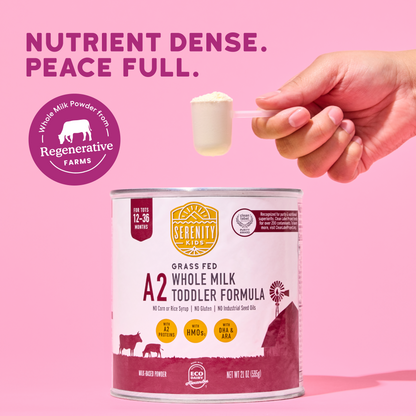 Serenity Kids A2 Grass Fed Whole Milk Toddler Formula can with a hand holding a spoonful of powder against a pink background.