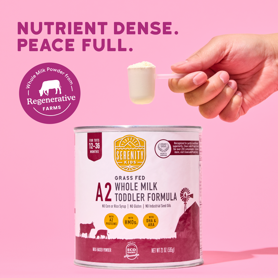Serenity Kids A2 Grass Fed Whole Milk Toddler Formula can with a hand holding a spoonful of powder against a pink background.