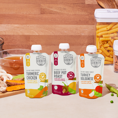 Three Serenity Kids bone broth food packaging on a wooden table with ingredients.
