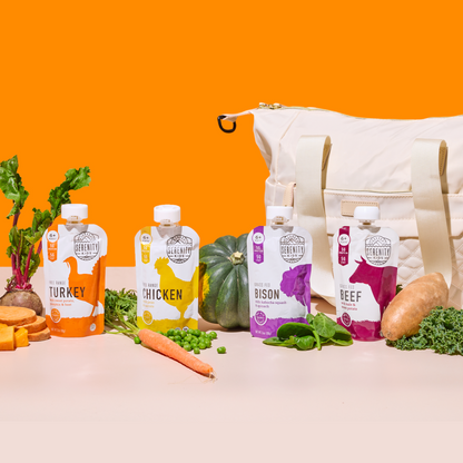 Four baby food packages on a beige surface with vegetables against an orange background.