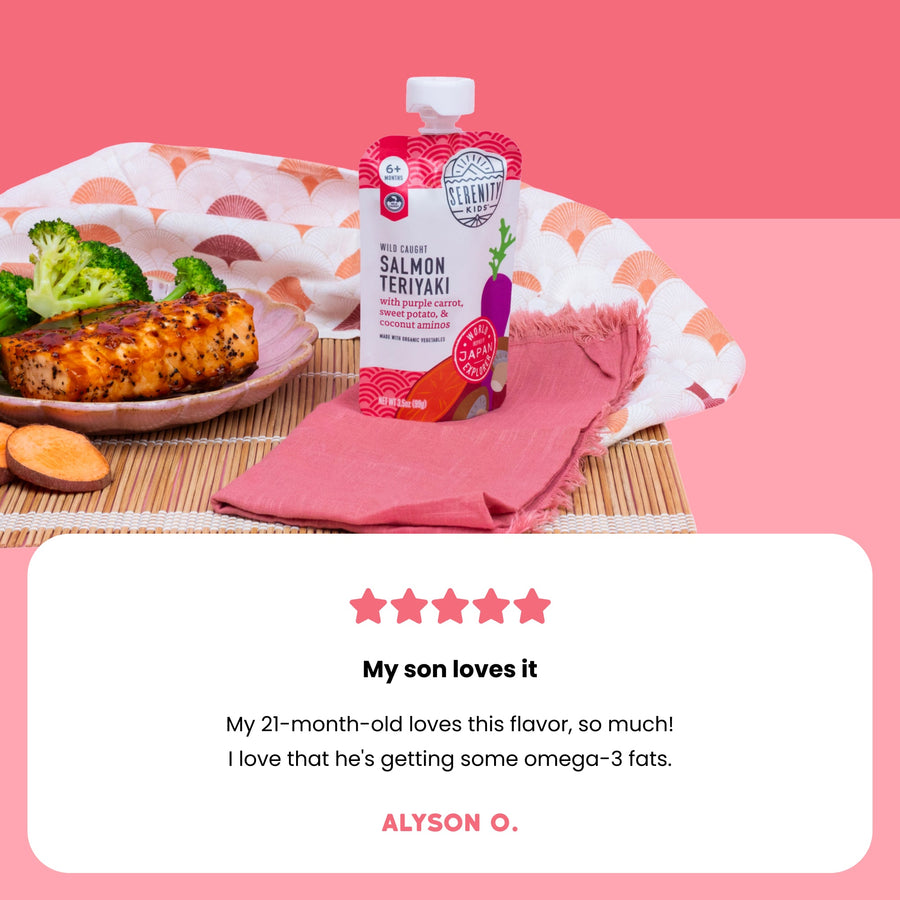 Baby food product on a table with salmon teriyaki flavor, surrounded by vegetables and a pink napkin and a customer review. 