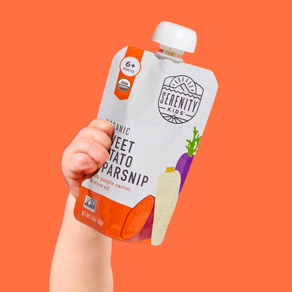 Hand holding a Serenity Kids organic sweet potato parsnip pouch against an orange background