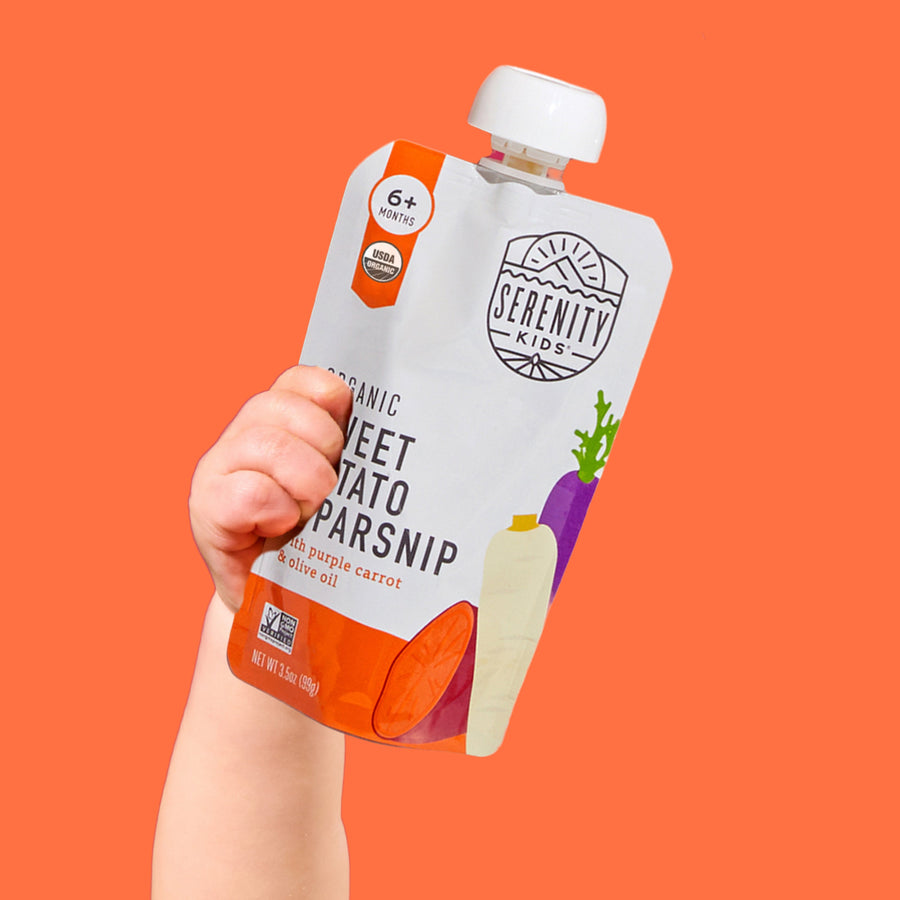 Hand holding a Serenity Kids organic sweet potato parsnip pouch against an orange background