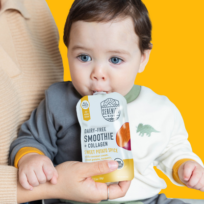 Baby holding a Serenity Kids Sweet Potato Spice smoothie pouch against a yellow background
