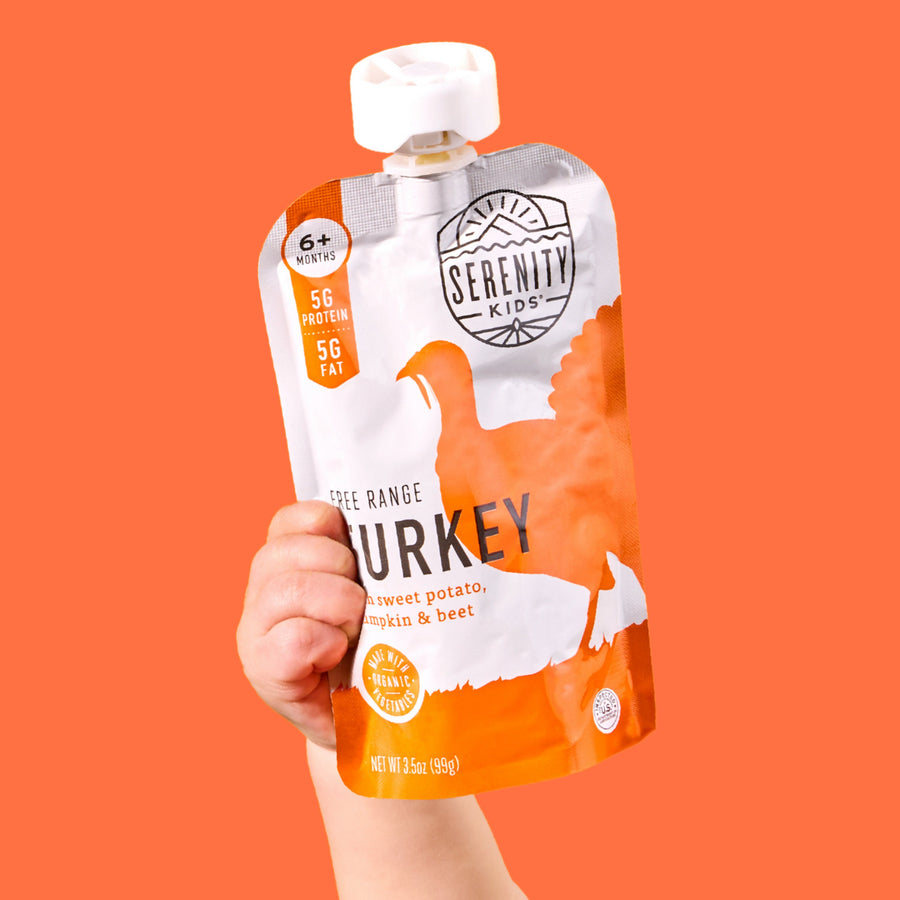 Hand holding a Serenity Kids turkey pouch against an orange background