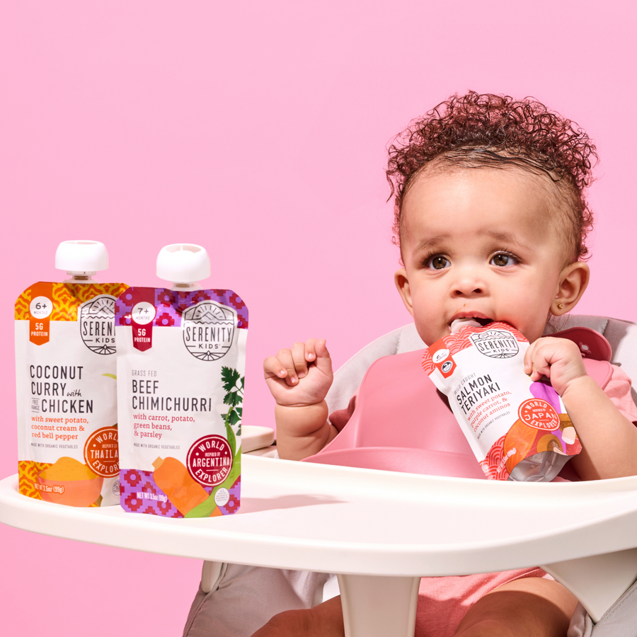 Baby in a high chair with Serenith Kids food pouches on a pink background