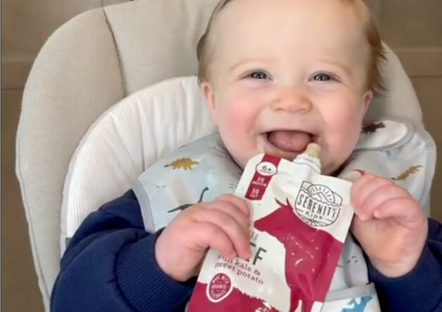 Smiling baby holding a Serenity Kids beef pouch